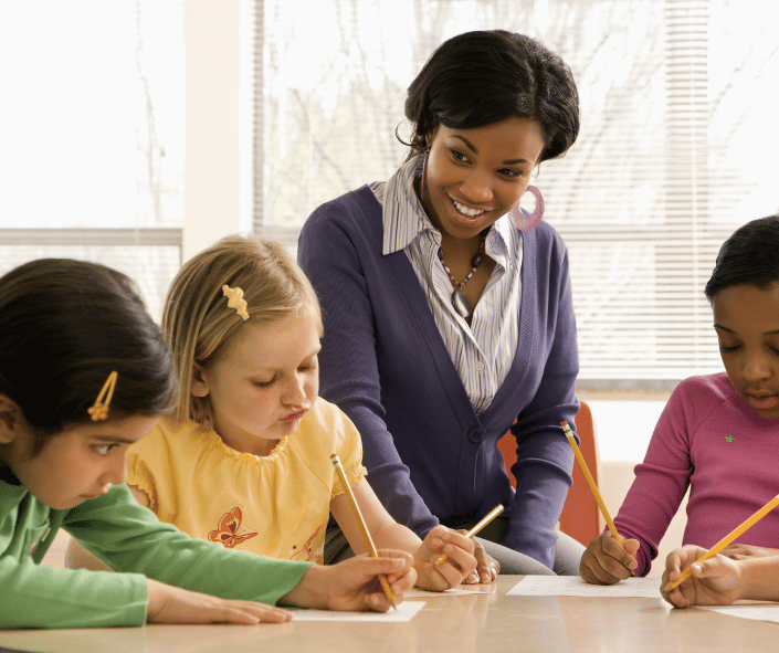 smiling teacher sitting with students at a desk