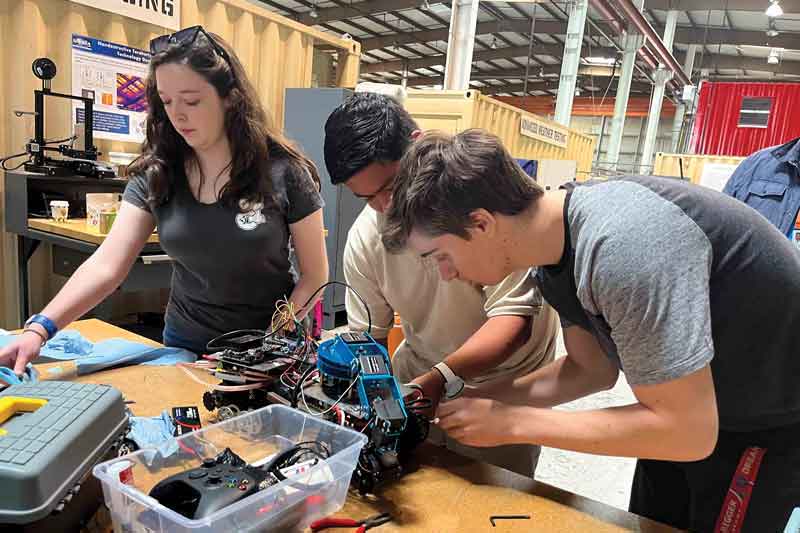Kenna Chase and Computer Science student Matthew Gonzalez and Mechantronics Engineering student Alex Marchand assemble the mechanics of a robot.