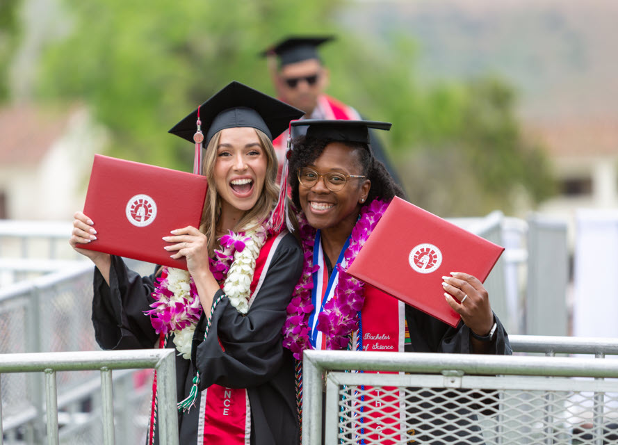 Two students graduating, smiling and holding up diplomas
